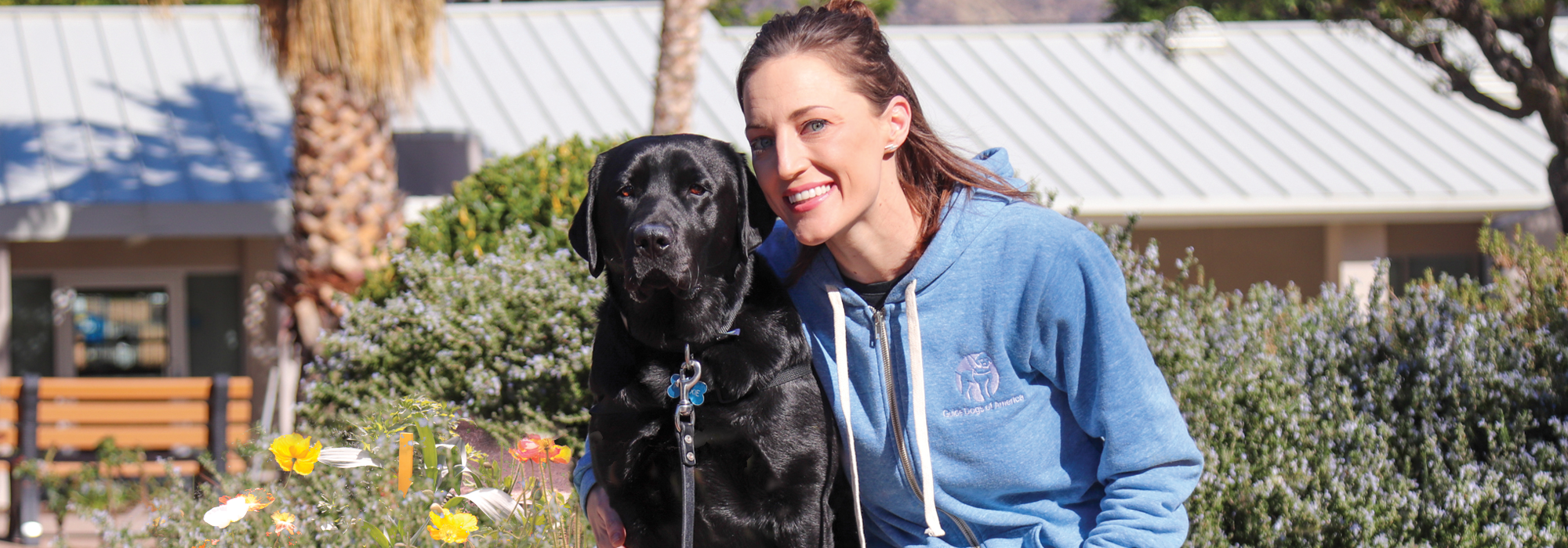 female veteran, black lab service dog, sitting on bench outside
